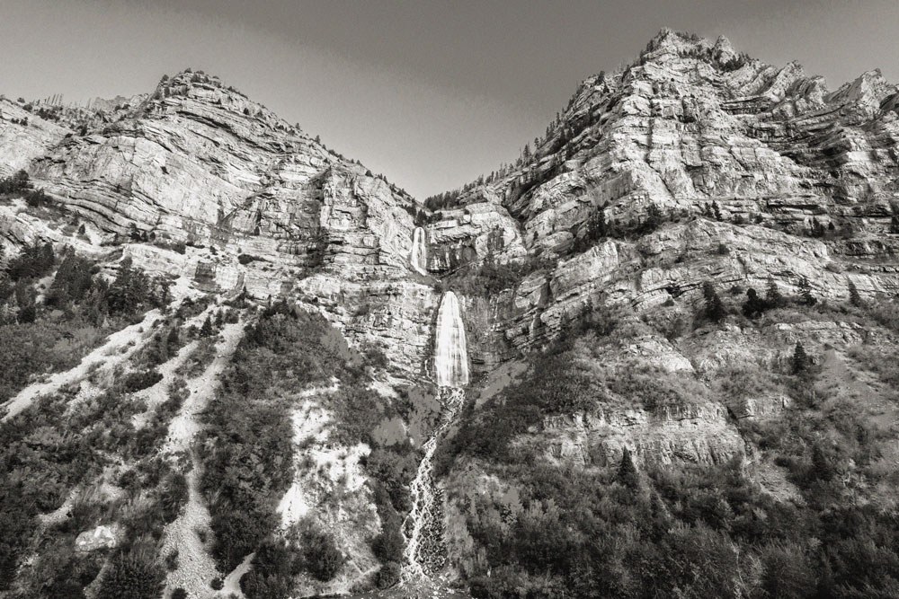 A black-and-white photograph of a two-tiered waterfall dropping between layered canyon cliffs