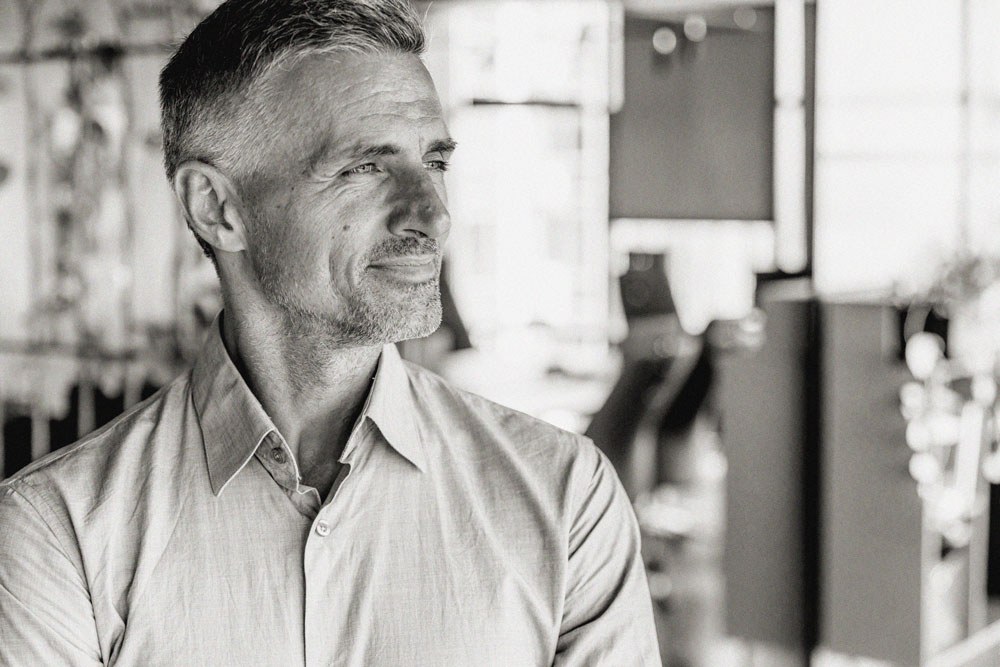 A business owner in an open-collared shirt looks thoughtfully across his workplace
